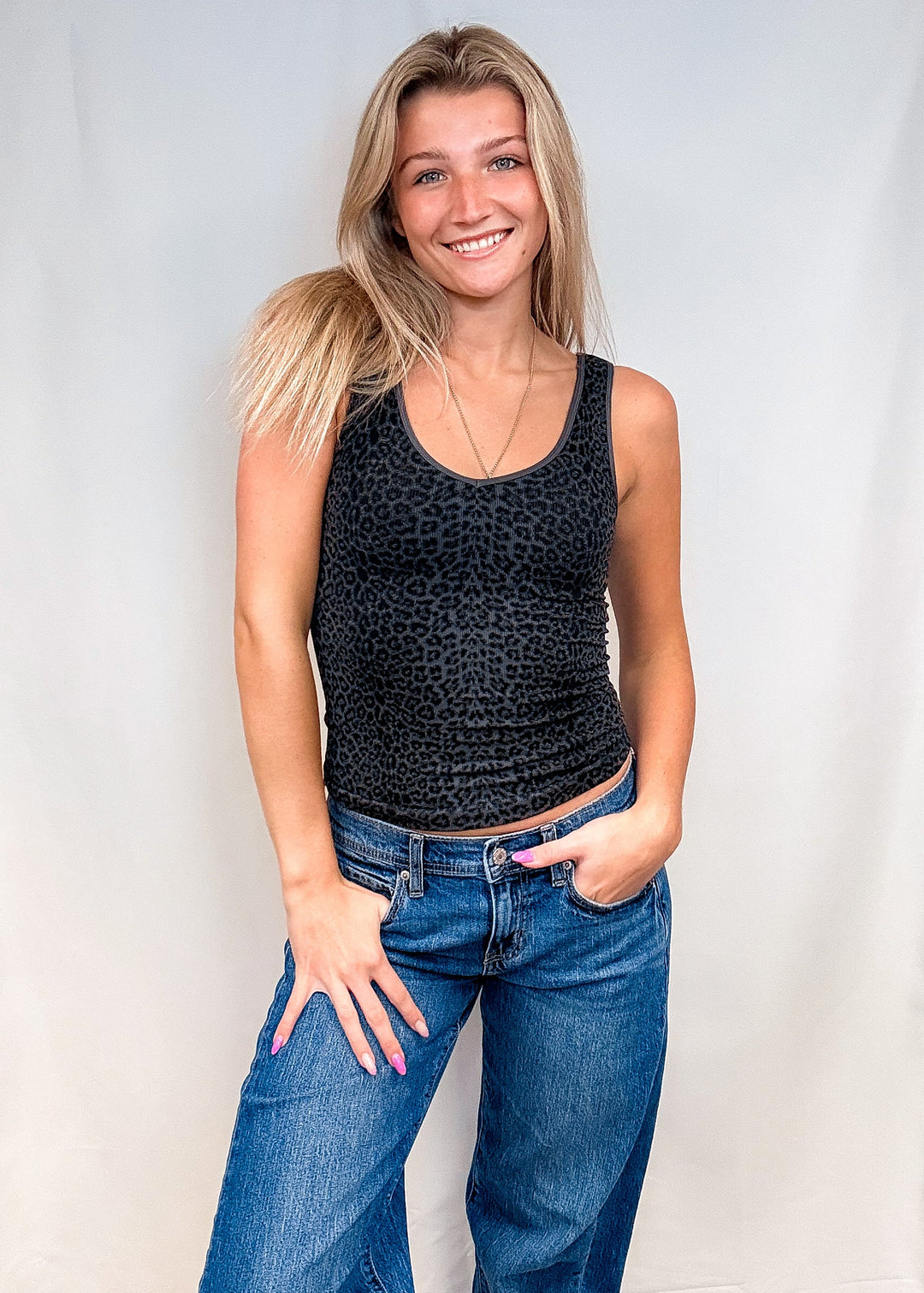 Woman wearing dark grey leopard print tank top with blue jeans on white background
