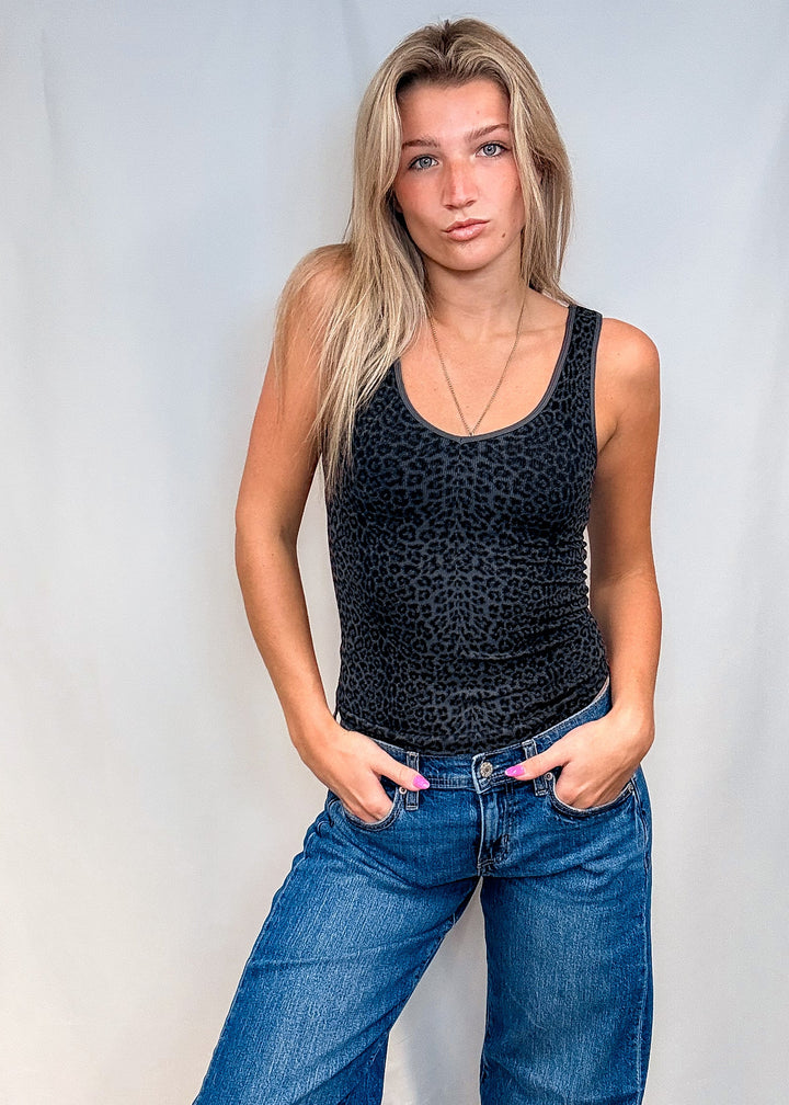 Woman wearing dark grey leopard print tank top with blue jeans on white background