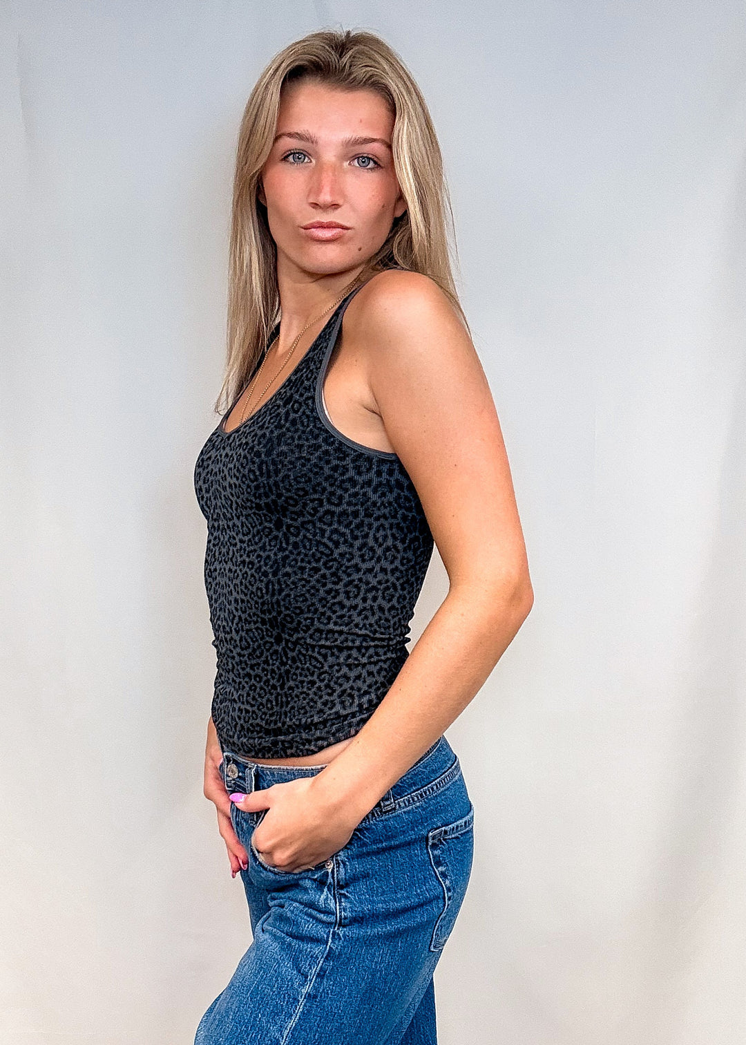 Woman wearing dark grey leopard print tank top with blue jeans on white background