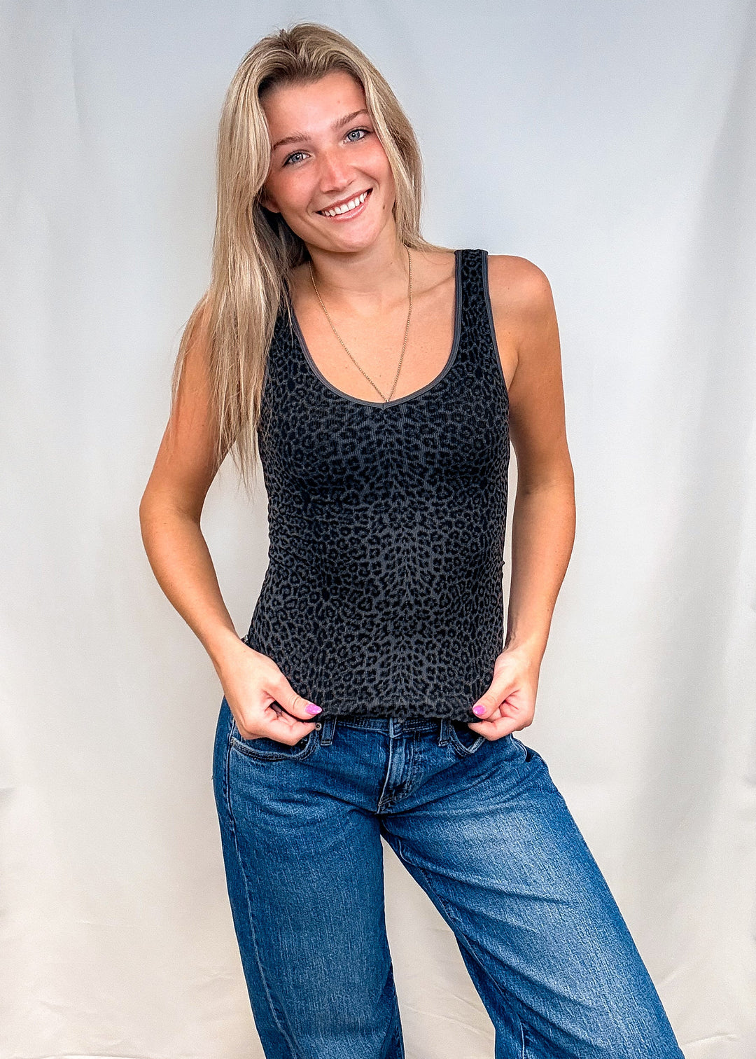 Woman wearing dark grey leopard print tank top with blue jeans on white background