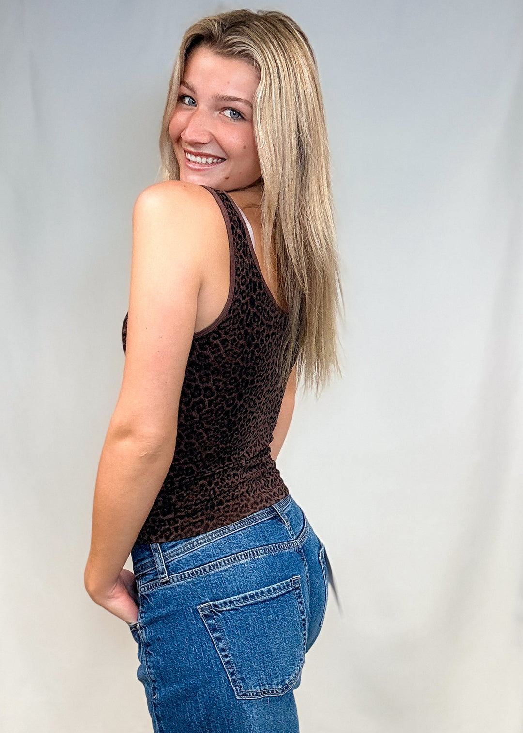 Woman wearing brown leopard print tank top with blue jeans on white background