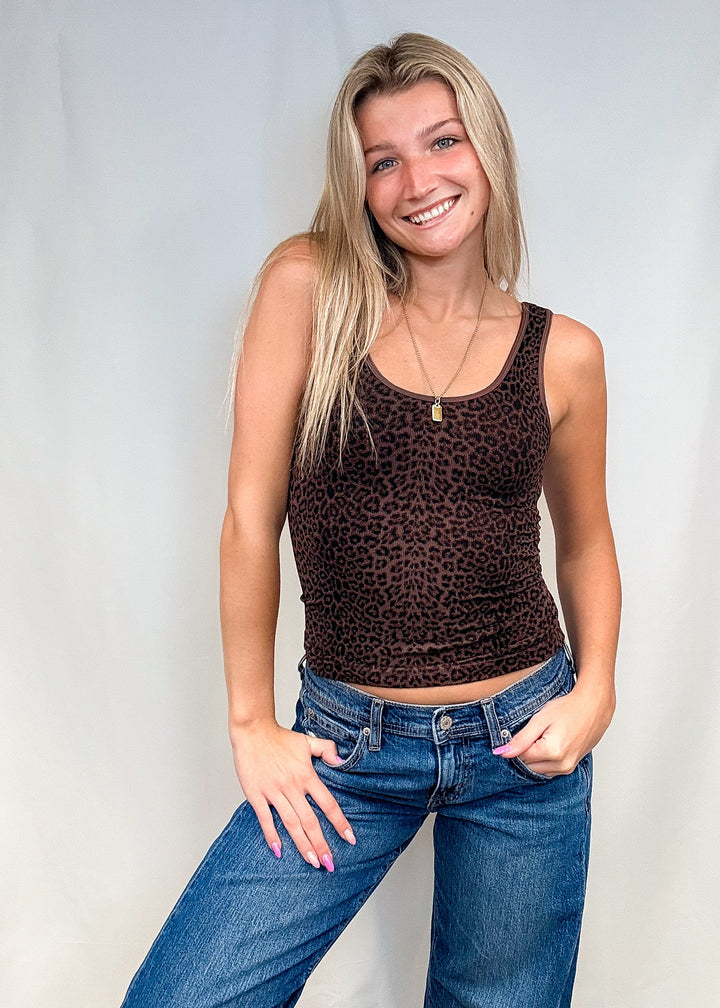 Woman wearing brown leopard print tank top with blue jeans on white background.