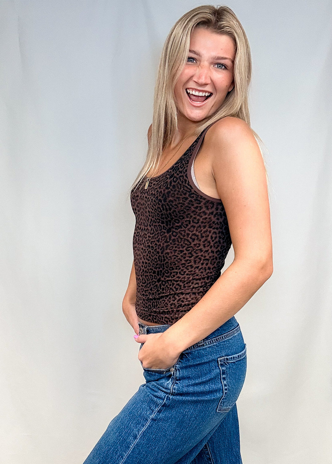 Woman wearing brown leopard print tank top with blue jeans on white background