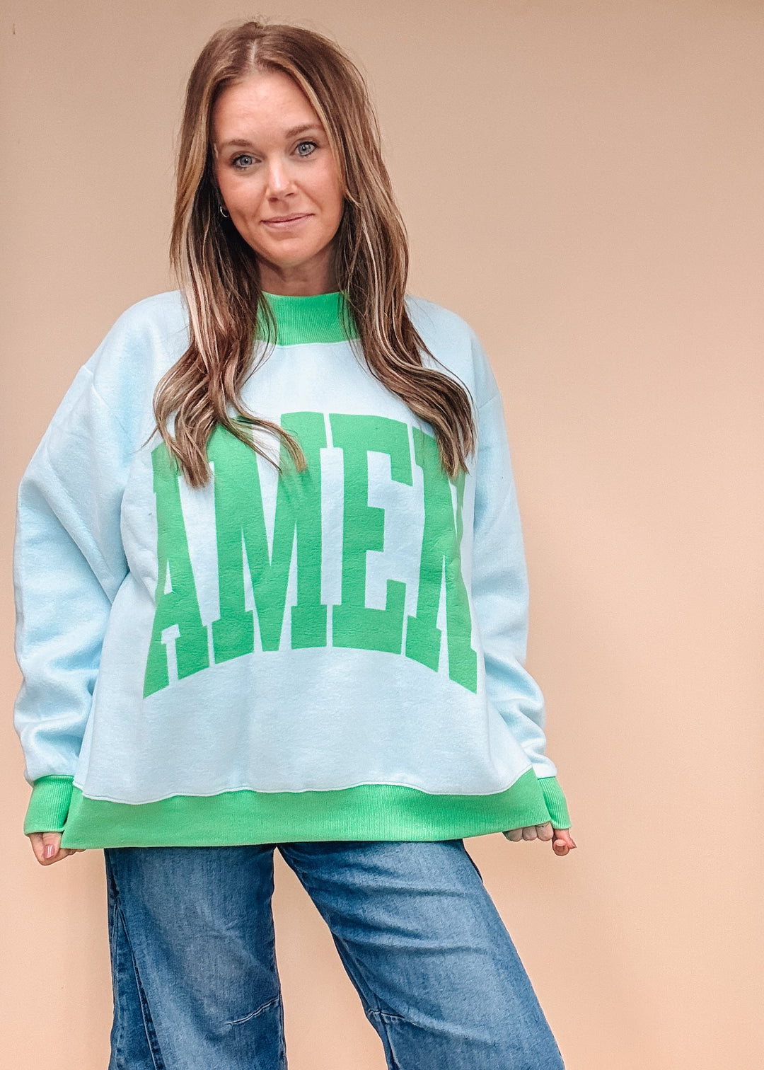 A woman modeling a light blue crewneck sweatshirt with green trim and a large green &
