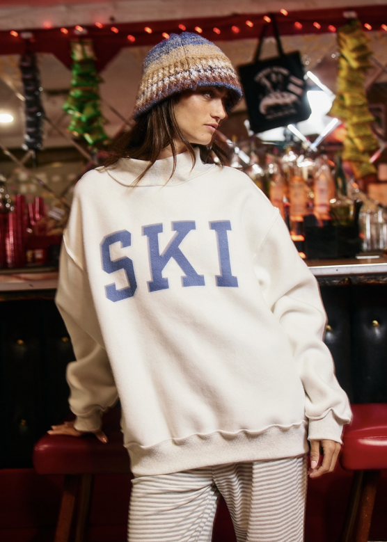 A woman wearing an oversized cream sweatshirt with &