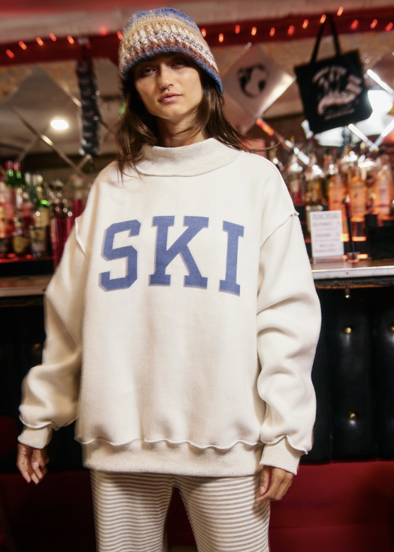 A woman wearing an oversized cream sweatshirt with &