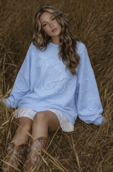 Woman wearing light blue pullover and white skirt sitting in grass
