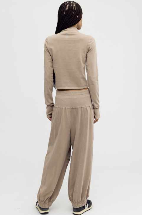 A model viewed from the back wearing a beige knit two-piece set consisting of a long-sleeve cropped top and matching wide-leg pants, paired with black and white sneakers against a plain white studio background.