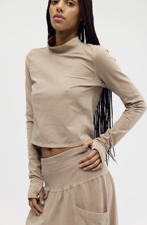 A model wearing a beige long-sleeve mock neck crop top and matching beige high-waisted pants against a plain white background.