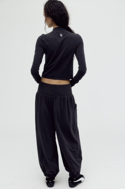 A model shown from the back wearing a black long-sleeve crop top and matching black wide-leg harem pants against a plain white studio background.