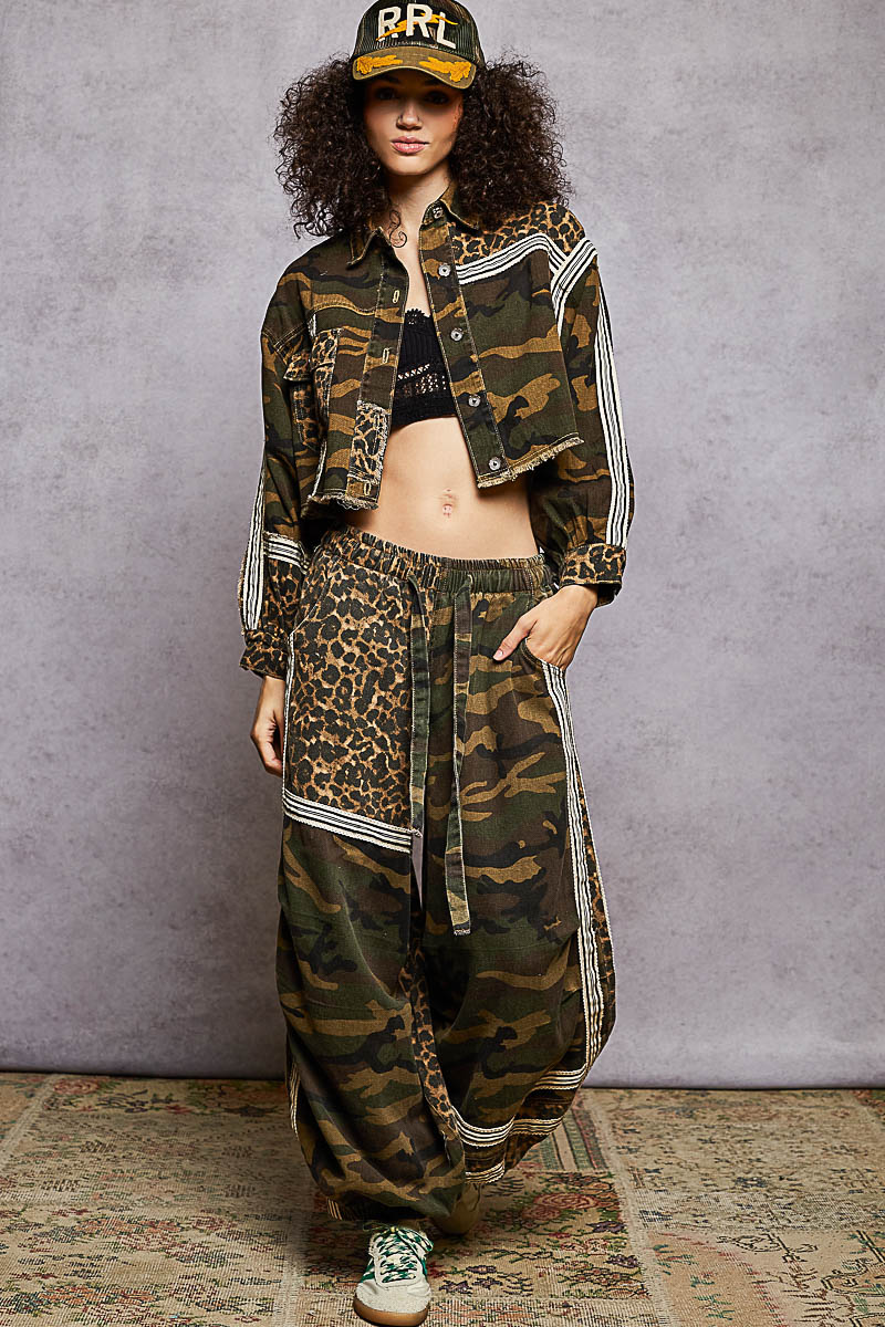 Person wearing a camouflage jacket and pants with a leopard print top against a gray background