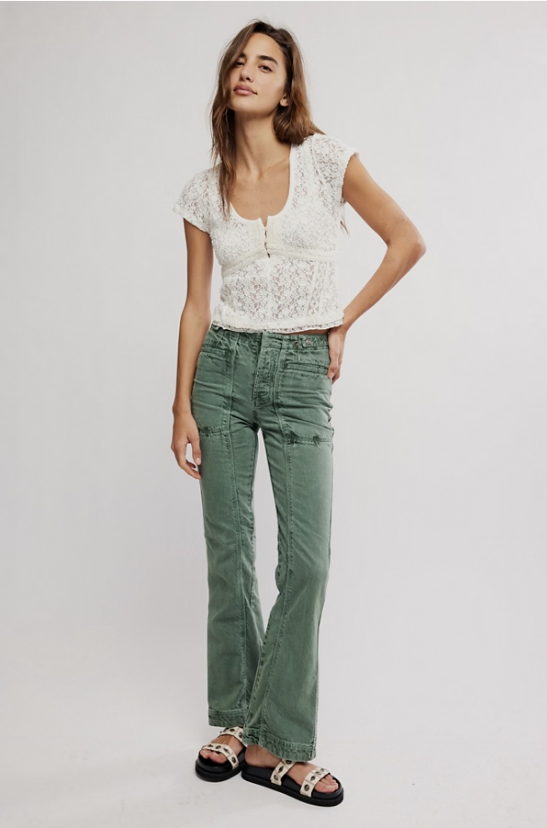 Woman wearing a white lace top and green pants on a plain background