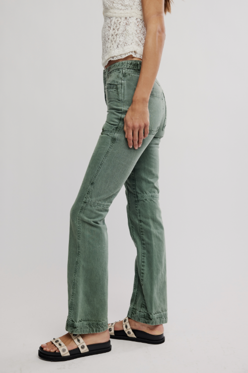 Person wearing green jeans and a white lace top on a plain background