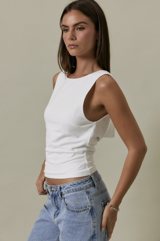 Woman wearing a white sleeveless top and blue jeans against a beige background