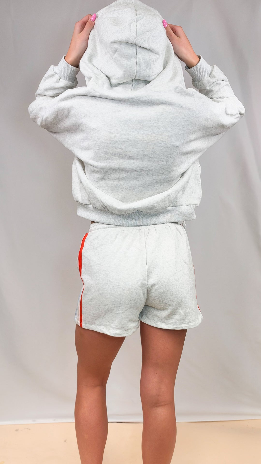 Woman shown from back wearing matching grey sweatsuit with hoodie and shorts on plain background