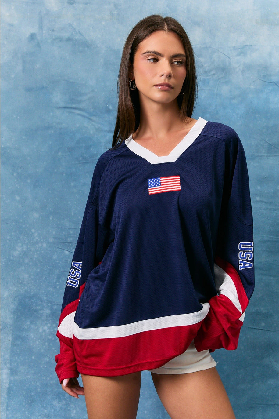 Woman wearing a navy blue long-sleeve shirt with USA flag design on a textured blue background
