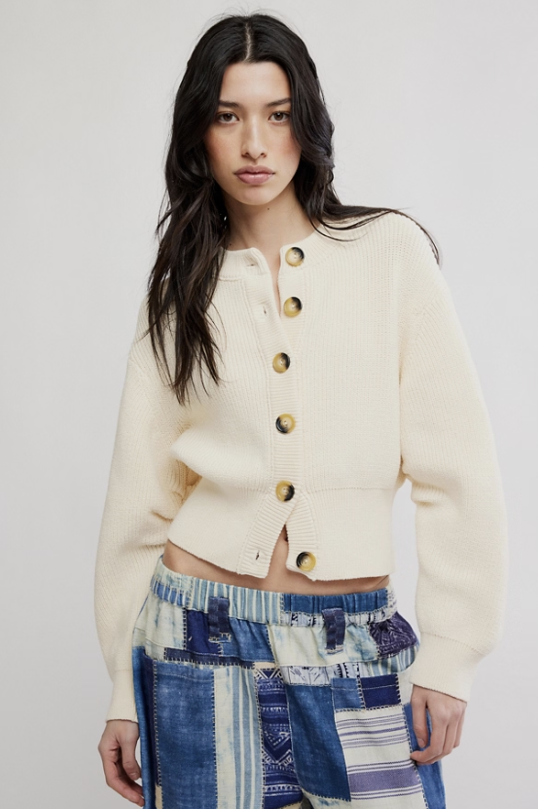 Woman wearing off white cardigan and blue patchwork pants on white background