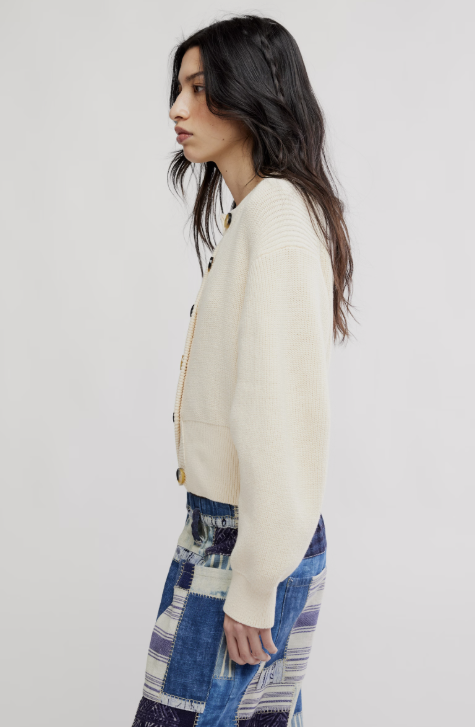 Woman wearing off white cardigan and blue patchwork pants on white background
