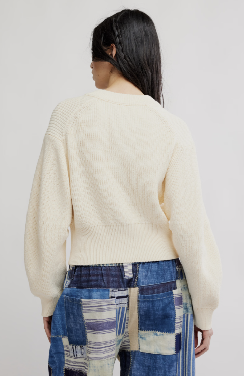 Woman wearing off white cardigan and blue patchwork pants on white background