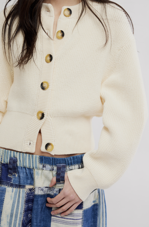 Woman wearing off white cardigan and blue patchwork pants on white background