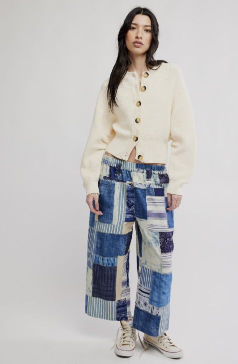 Woman wearing off white cardigan and blue patchwork pants on white background
