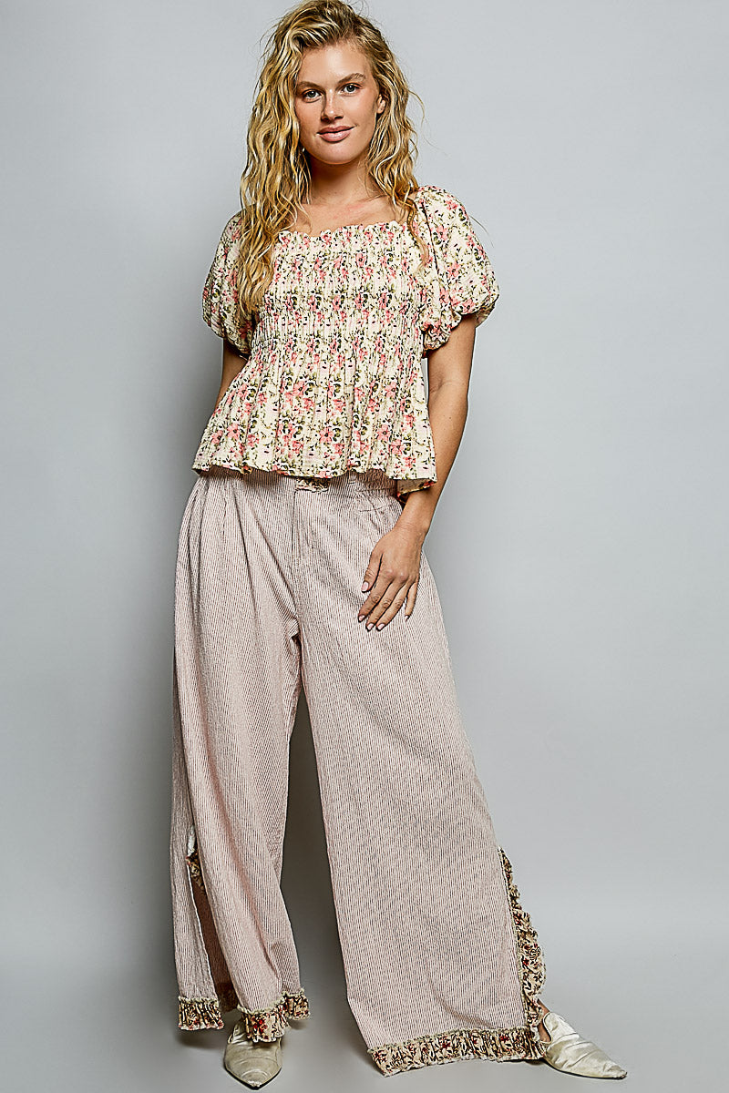 Woman wearing a floral top and beige pants against a gray background