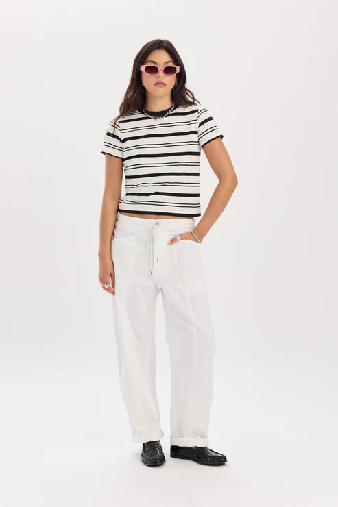 Woman wearing a black and white striped crop top with white pants on a white background