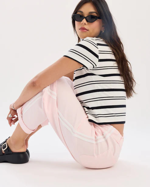 Woman wearing a striped shirt and pink pants sitting on a white background