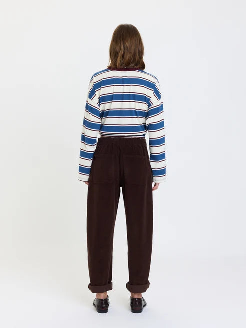A model viewed from the back wearing a blue, white, and navy striped long-sleeve crop top and dark brown corduroy trousers, set against a plain white studio background.