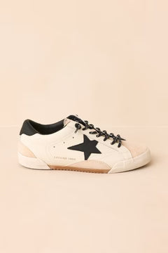 White sneaker with black star and sole on a beige background