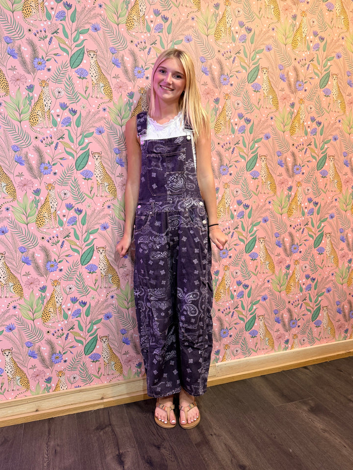 Person wearing a dark patterned outfit standing against a pink wall with animal and floral designs.