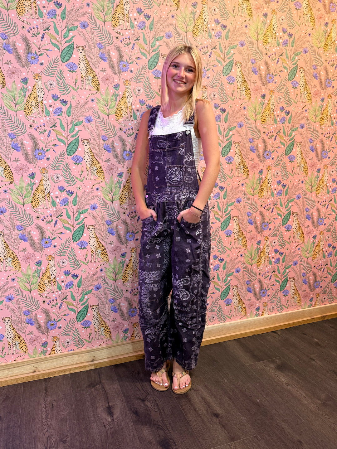 Person wearing a dark patterned outfit standing in front of a pink floral wallpapered wall.