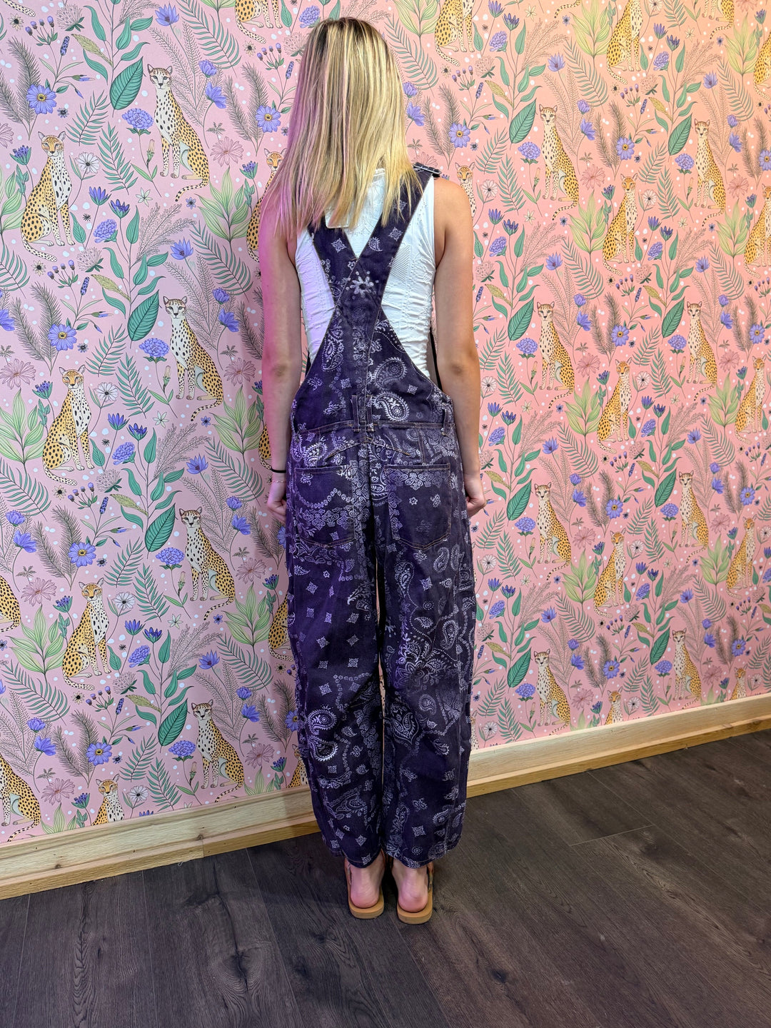 Person wearing a patterned jumpsuit standing in front of a wall with a colorful animal and floral design.