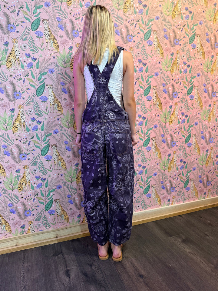 Person wearing a patterned jumpsuit standing in front of a wall with a colorful animal and floral design.