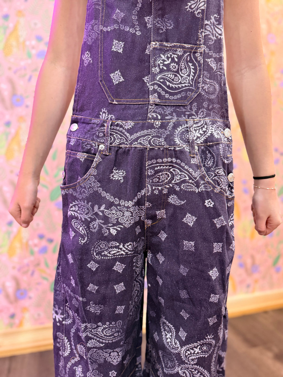 Purple bandana-patterned overalls worn by a person against a colorful, abstract background.