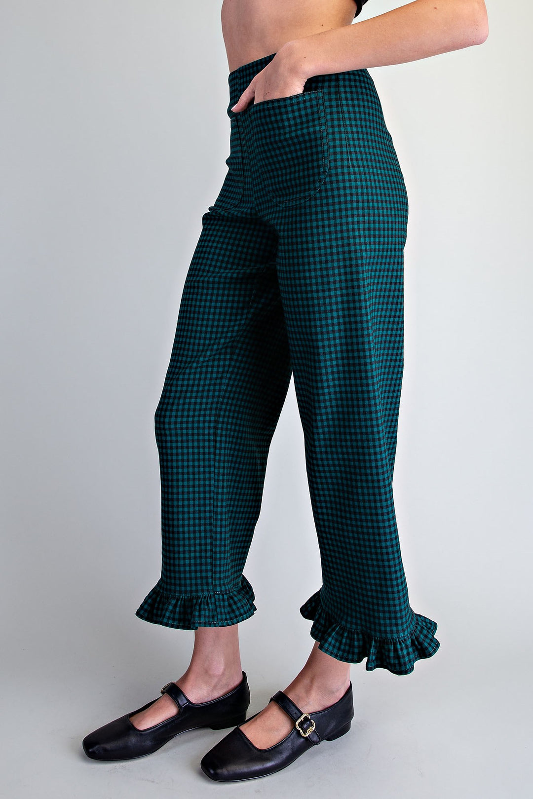 A person wearing dark green and black gingham cropped pants with ruffled hems, paired with black Mary Jane shoes, shown against a light gray studio background.
