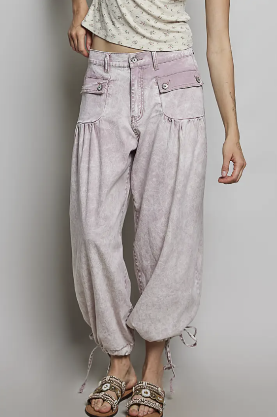 A person wearing light lavender-purple harem-style jeans with drawstring ankle cuffs, shown from the waist down against a plain light gray studio background.