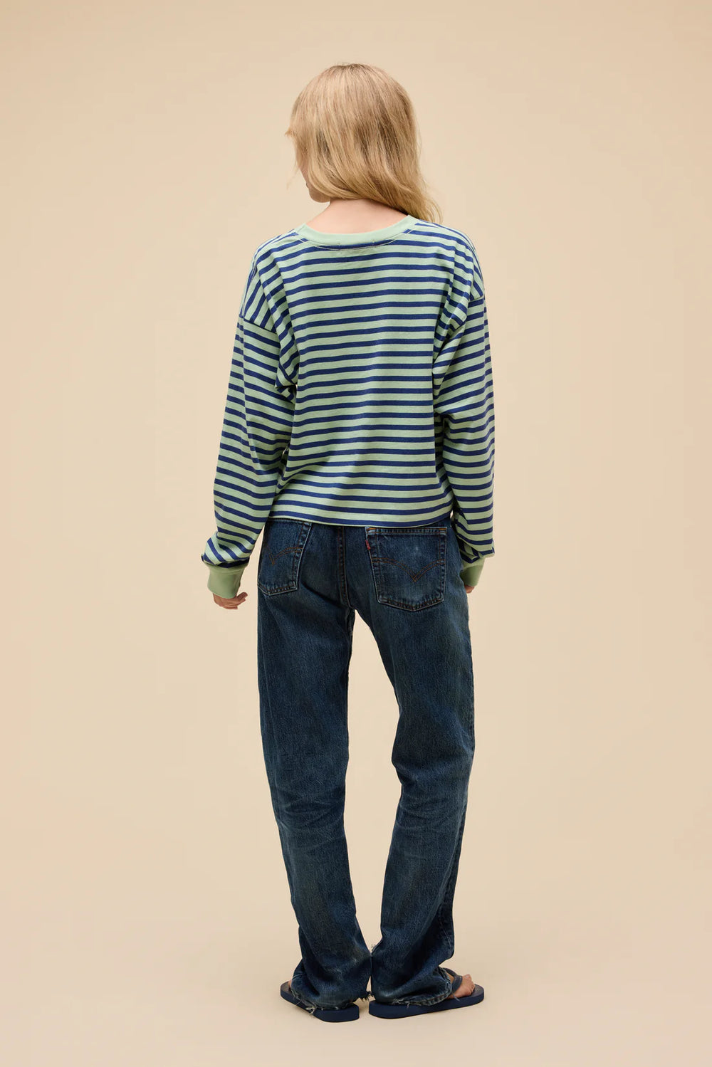 Person wearing a striped sweater and blue jeans on a beige background
