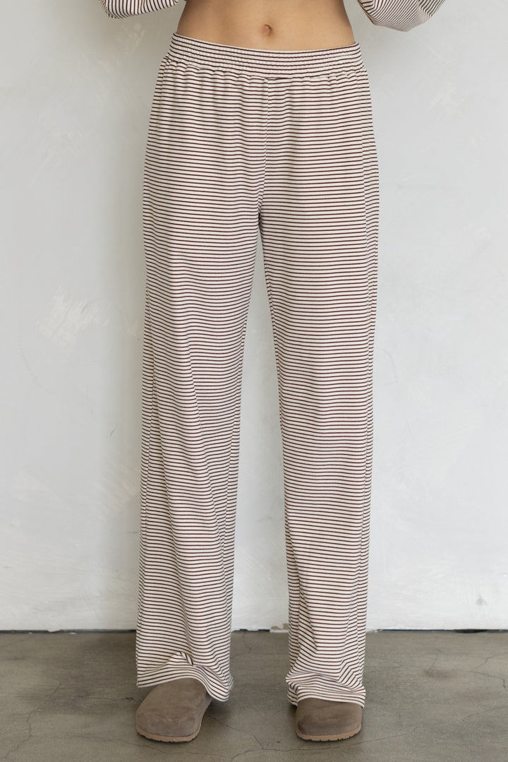 A person wearing loose, wide-leg pants with thin horizontal beige and brown stripes, standing against a plain light wall.