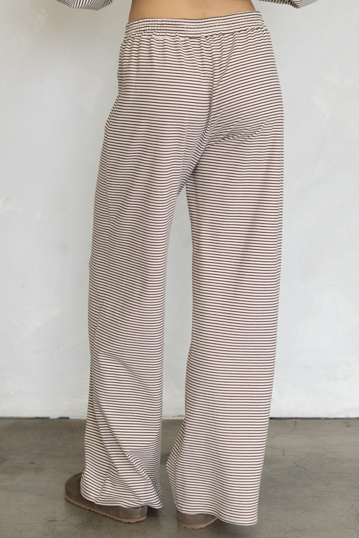 A person wearing loose, wide-leg pants with thin horizontal beige and brown stripes, shown from the waist down against a plain light wall.