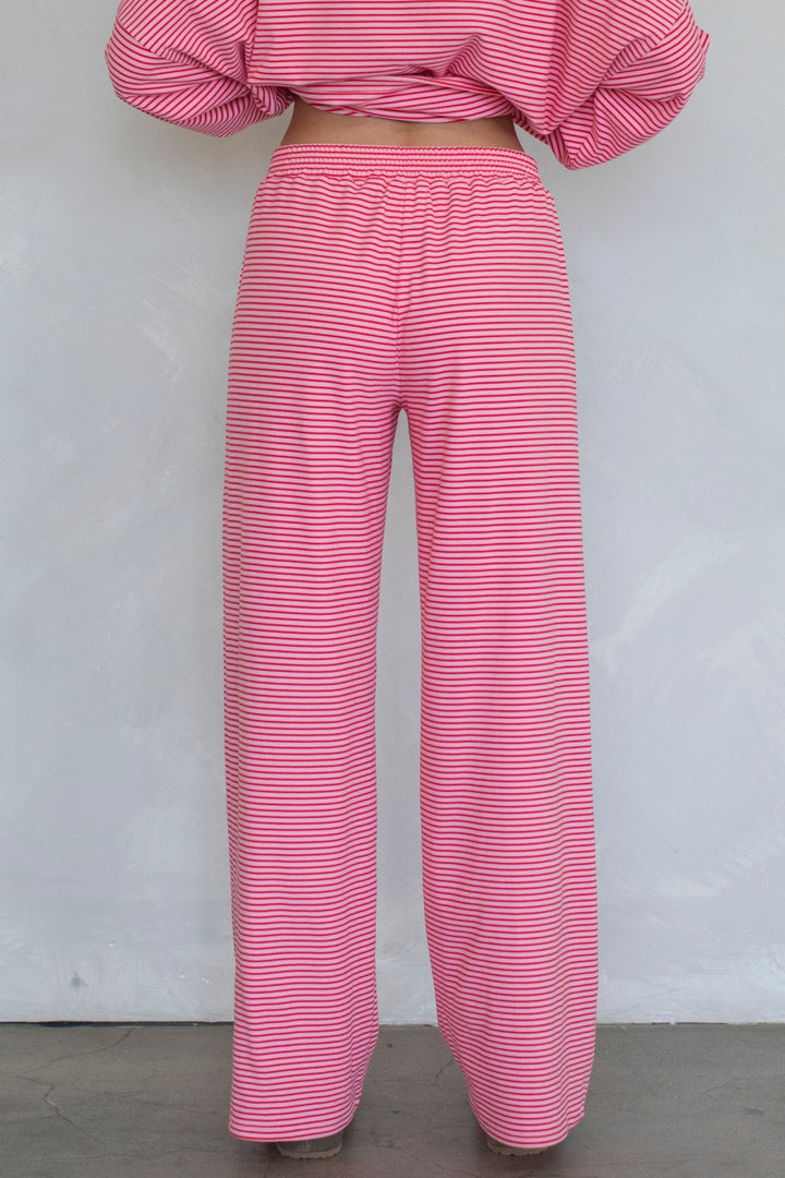 Pink and white striped wide-leg pants shown from the back on a model, paired with a matching striped top against a plain light gray wall.