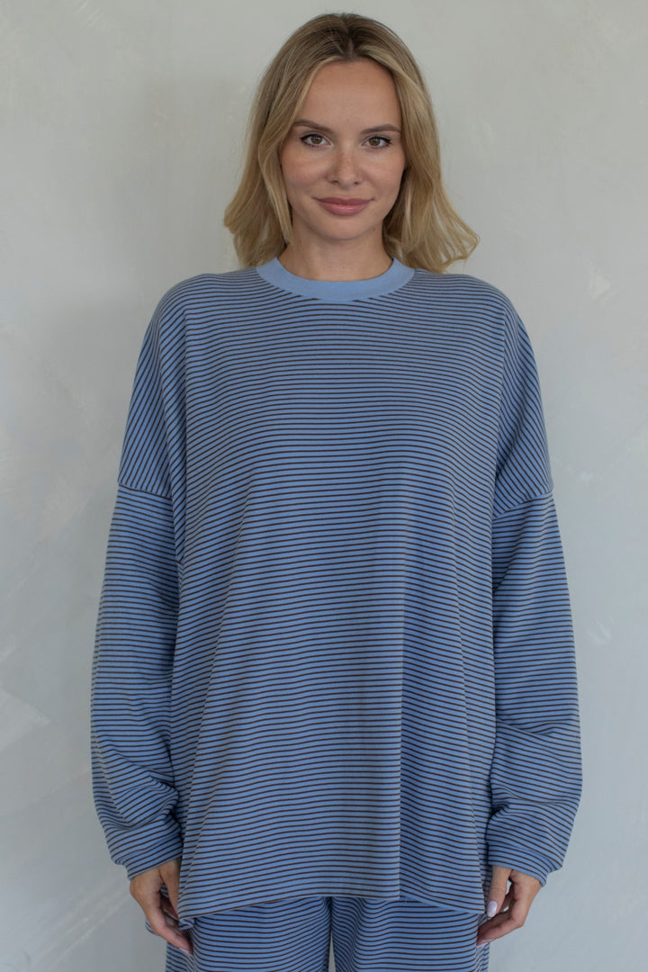 Woman wearing a blue striped sweater and pants against a plain background