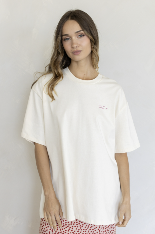 A woman wearing an oversized off-white t-shirt with a small pink &