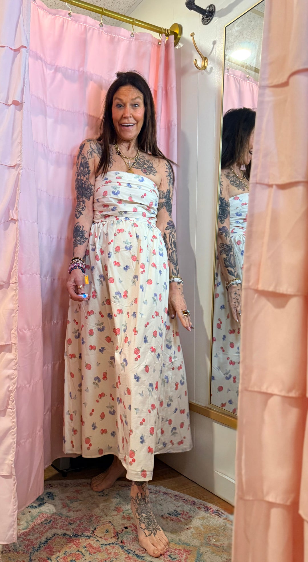 Woman in a floral dress standing in front of a mirror with pink curtains.