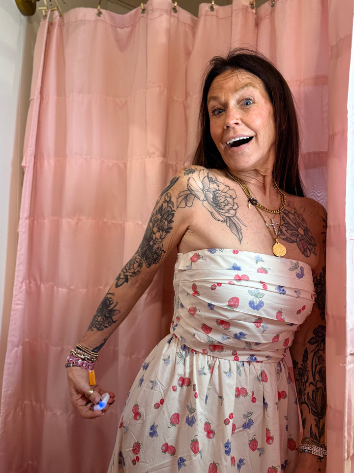 Woman with tattoos wearing a floral dress in front of a pink curtain