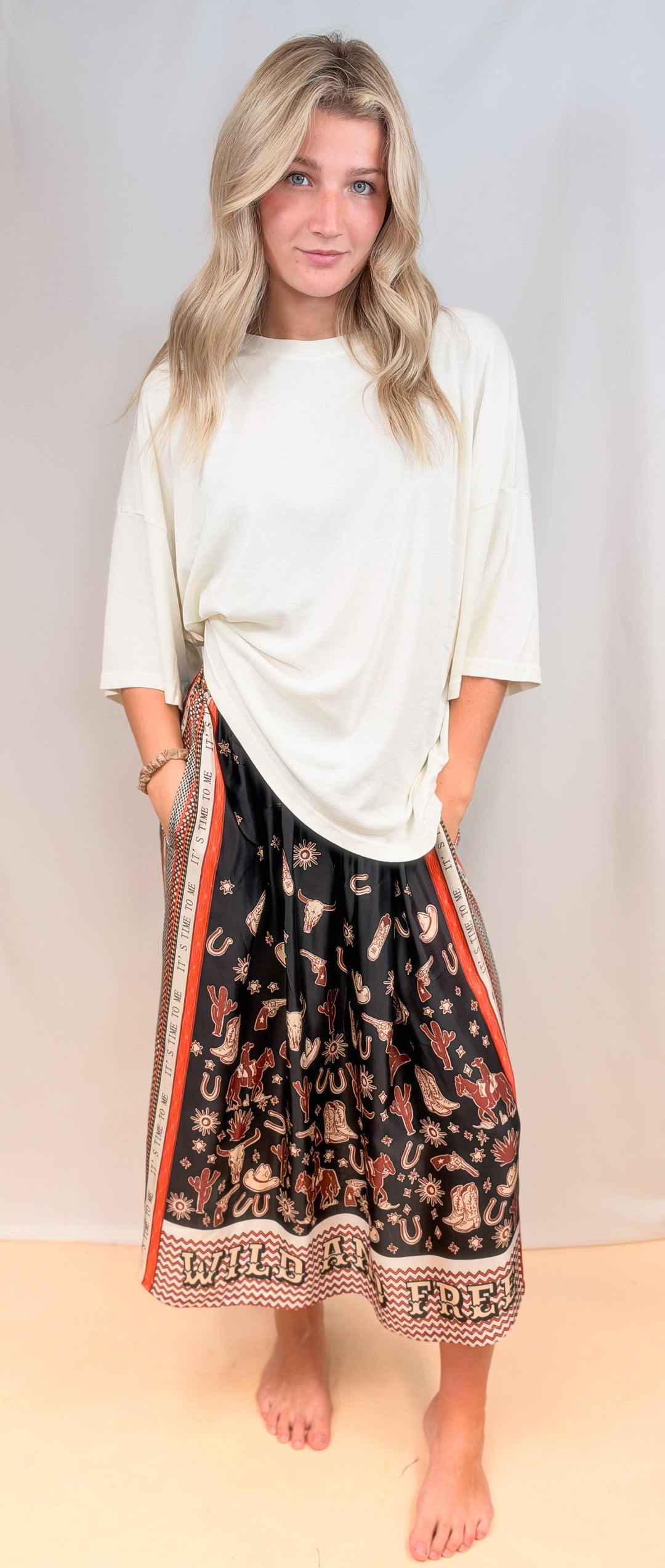 Woman wearing white tee with rodeo motif scarf skirt on plain background