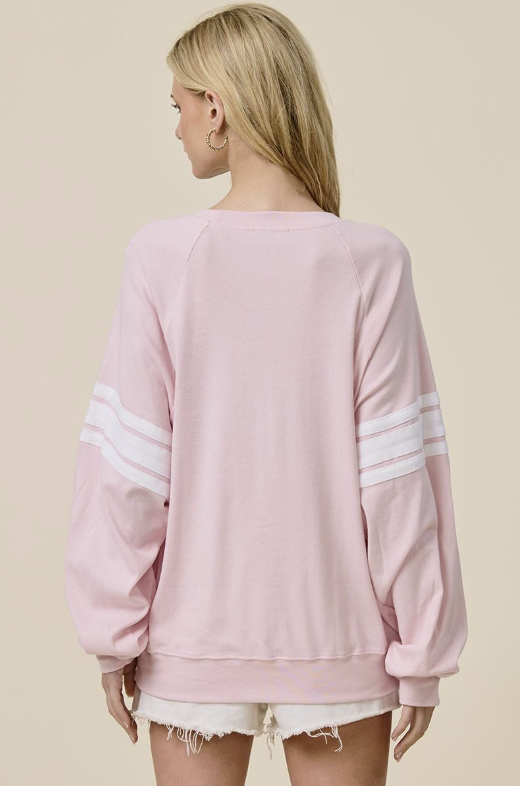 A woman shown from the back wearing a light pink crewneck sweatshirt with white stripes on the sleeves, paired with white frayed denim shorts, against a solid beige background.