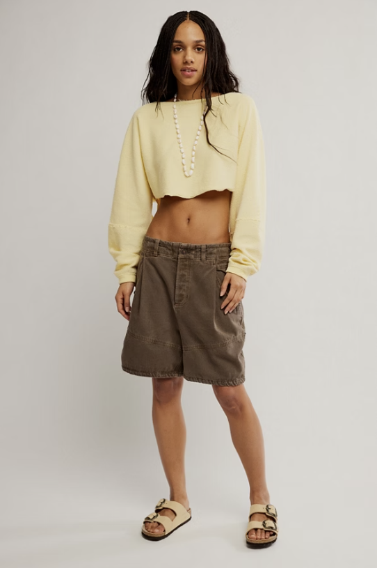 Woman wearing brown shorts and yellow cropped sweater on plain background