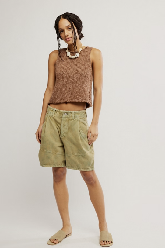 Woman wearing a brown sleeveless top and green shorts on a plain background