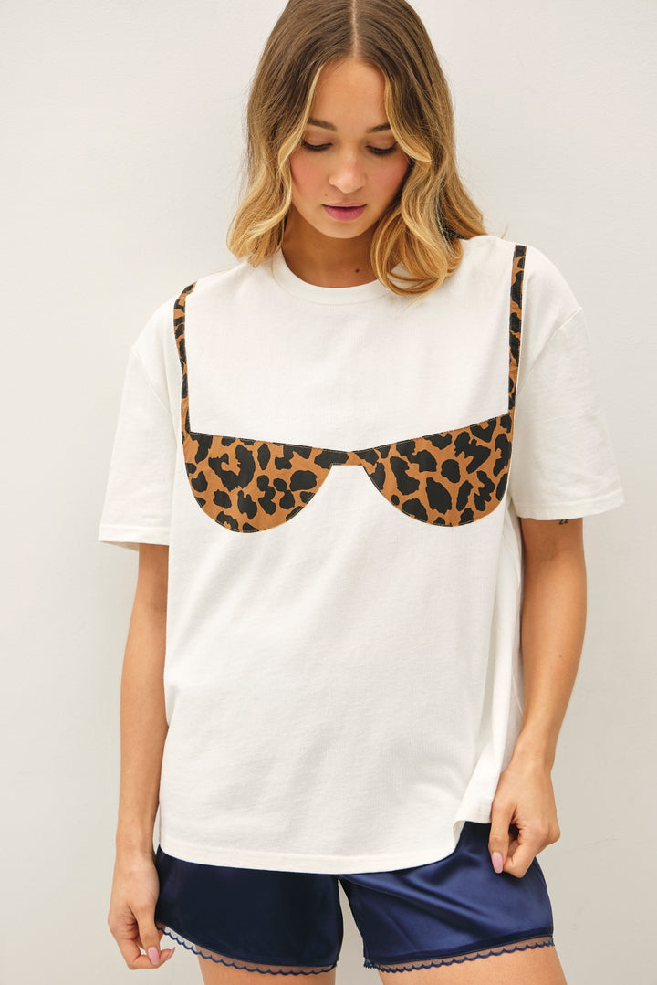 Woman wearing white tee with leopard print bathing suit detail on plain background